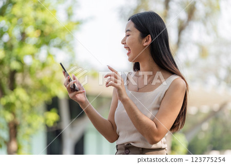 Digital connection. Woman smiling while using her smartphone outdoors. 123775254