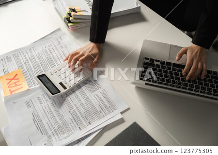 Businesswoman using a calculator for tax calculations while managing financial documents. 123775305