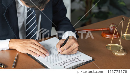 Lawyer reviewing and signing contract documents with gavel and scales of justice on desk. 123775376