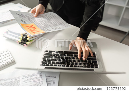 Businesswoman reviewing tax documents while using a laptop in the office. 123775392