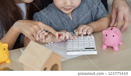 Child learning about finances with parents using a calculator and piggy banks 123775410