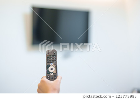hand using remote controller press button for adjust Smart TV in modern room at home. Woman holding remote control, switch channel, searching new interesting program, Turn on or off on Television hand using remote controller press button for adjust Smart TV in modern room at home. Woman holding remote control, switch channel, searching new interesting program, Turn on or off on Television 123775983