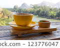 Yellow coffee cup and coffee spoon on wooden table with scenic mountain and river view. 123776047