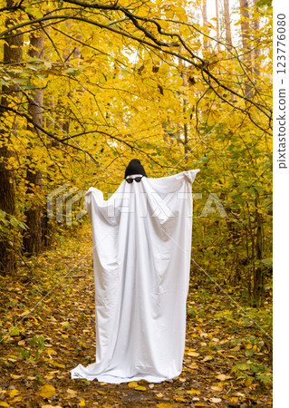 Happy Halloween holiday. Cute unrecognizable person dancing in ghost costume on fall forest background. Creative costume with white and black cap hat and glasses Happy Halloween holiday. Cute unrecognizable person dancing in ghost costume on fall forest background. Creative costume with white and black cap hat and glasses 123776080