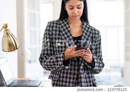 Professional woman in business attire is using a smartphone multitasking 123776125