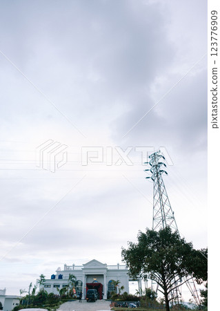 Electricity tower with trees and a white building under a cloudy sky in a suburban landscape Electricity tower with trees and a white building under a cloudy sky in a suburban landscape 123776909