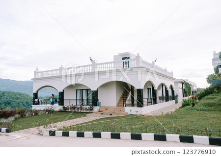White colonial-style building with a lush garden and pathway under a bright, cloudy sky. White colonial-style building with a lush garden and pathway under a bright, cloudy sky. 123776910