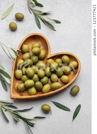 Fresh green olives displayed on wooden heart shaped bowl with olive branches 123777421