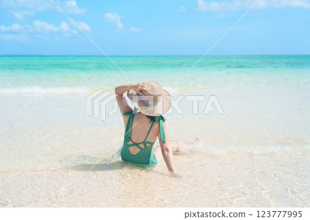 Happy Woman tourist in green swimwear and hat relaxing on beach, young solo traveller looking beautiful sea view on tropical island. Southeast Asia destination, summer Travel, vacation and holiday 123777995