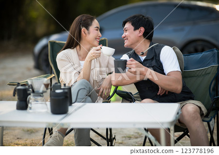 A woman and man is smiling at each other while holding their cup at folding table on camping ground A woman and man is smiling at each other while holding their cup at folding table on camping ground 123778196