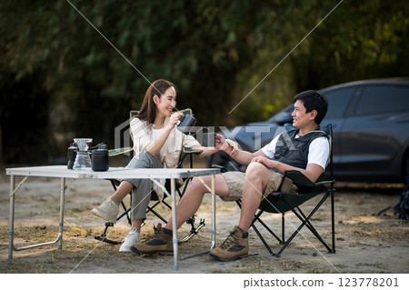 A girlfriend is holding boyfriend wrist while pouring drink at the folding table on camping ground. 123778201
