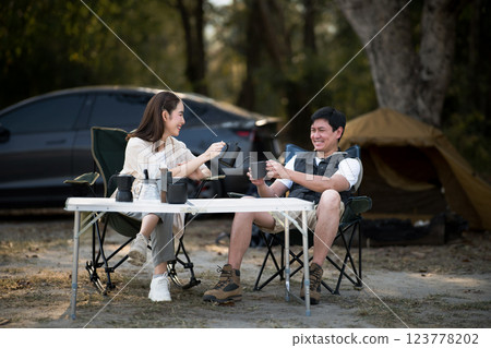 A woman is smiling while pouring drink for the man at folding table in front of their camping tent. 123778202