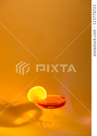 glass of champagne with a slice of orange on an orange background, with shadows 123778722