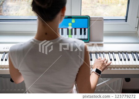 Young woman learning to play the keyboard at home using an interactive app. Using mobile apps for self-study concept Young woman learning to play the keyboard at home using an interactive app. Using mobile apps for self-study concept 123779272