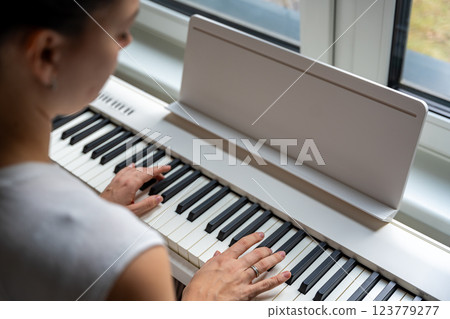 Young woman playing a keyboard at home. Music practice enhances creativity and emotional expression Young woman playing a keyboard at home. Music practice enhances creativity and emotional expression 123779277