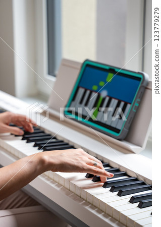 Hands playing a keyboard while following an interactive learning app on a tablet. Technology enables self-education in music without traditional lessons. Hands playing a keyboard while following an interactive learning app on a tablet. Technology enables self-education in music without traditional lessons. 123779279