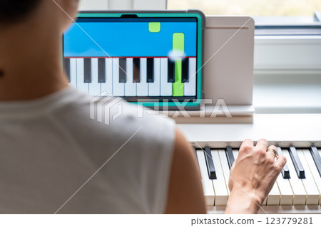 Close up view of young woman learning to play the keyboard at home using an interactive app. Using mobile apps for self-study concept 123779281