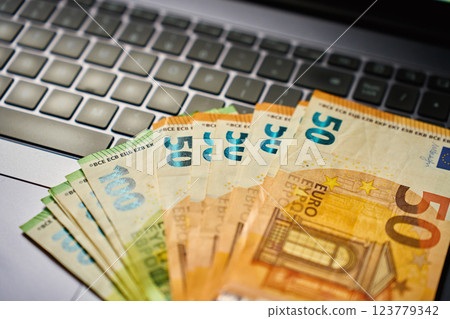 Euro banknotes on laptop keyboard. Concept of cash money, digital payments and financial transactions Euro banknotes on laptop keyboard. Concept of cash money, digital payments and financial transactions 123779342