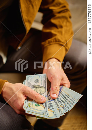 Close-up of man counting dollar banknotes at home. Person planning his personal finances, sitting on sofa with cash money. Concept of planning home budget, savings and personal finances Close-up of man counting dollar banknotes at home. Person planning his personal finances, sitting on sofa with cash money. Concept of planning home budget, savings and personal finances 123779356