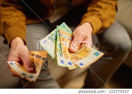 Person counting euro banknotes at home. Person planning his personal finances, sitting on sofa with cash money. Concept of planning home budget, savings and personal finances Person counting euro banknotes at home. Person planning his personal finances, sitting on sofa with cash money. Concept of planning home budget, savings and personal finances 123779357