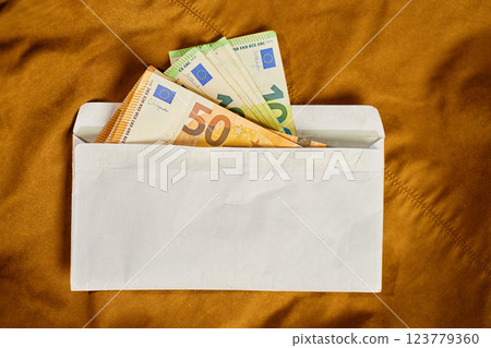 Euro banknotes inside white envelope, top view. Close up of cash money on brown background. Concept of corruption, bribery, and hidden cash payments 123779360