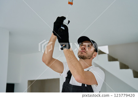 Professional electrician wearing gloves installing light bulb in ceiling socket. Home electrical work during renovation 123779420