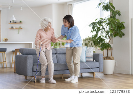 Care staff supporting a senior woman standing up with a cane 123779888