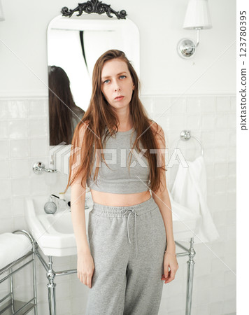 Young and sleepy woman with long hair in pajamas stands against the background of a sink in the bathroom. Lack of sleep and stress in women. Young and sleepy woman with long hair in pajamas stands against the background of a sink in the bathroom. Lack of sleep and stress in women. 123780395