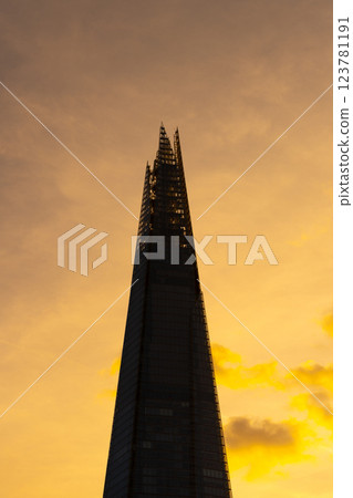 The Shard skyscraper stands tall against a vibrant sunset in London, casting its distinctive silhouette. The warm hues highlight the architectural elegance of this landmark. 123781191
