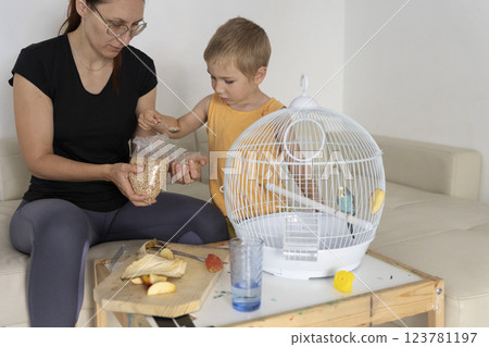 Mother and son feeding pet budgie bird in cage Mother and son feeding pet budgie bird in cage 123781197