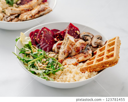 Bowl with grilled chicken, mushrooms, beetroot, quinoa, green rucola, decorated pine nuts and carrot waffle. Top view of gourmet bowl. Balanced gourmet dish on black wooden background. Healthy Food 123781455