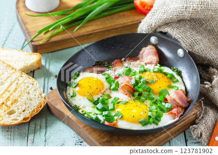 Spring scrambled eggs with green onions and bacon in a cast iron skillet on a rustic wooden background. 123781902