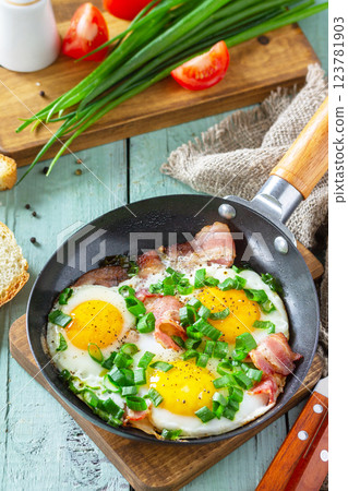 Spring scrambled eggs with green onions and bacon in a cast iron skillet on a rustic wooden background. 123781903