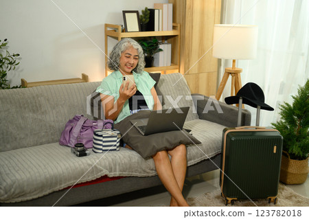 Smiling older woman with headphones holding a smartphone preparing for vacation Smiling older woman with headphones holding a smartphone preparing for vacation 123782018