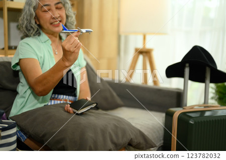 Cheerful senior woman holding a airplane model and passport preparing for summer trip in a home 123782032