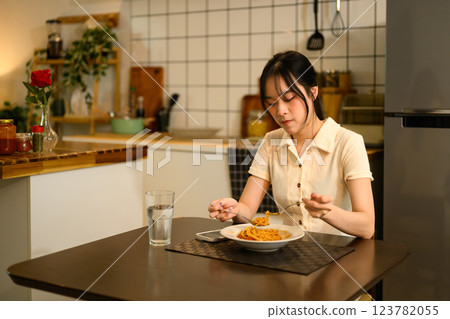 Young woman enjoys a plate of spaghetti at dining table in a cozy kitchen Young woman enjoys a plate of spaghetti at dining table in a cozy kitchen 123782055