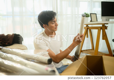Young man unpacking furniture part, ready to assemble furniture in his living room Young man unpacking furniture part, ready to assemble furniture in his living room 123782057