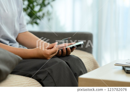 Young woman holding smartphone and credit card, making an online purchase in living room Young woman holding smartphone and credit card, making an online purchase in living room 123782076