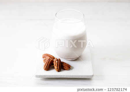 Pecan milk in a glass with raw pecan nuts on wooden table. Pecan milk in a glass with raw pecan nuts on wooden table. 123782174