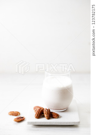 Pecan milk in a glass with raw pecan nuts on wooden table. Pecan milk in a glass with raw pecan nuts on wooden table. 123782175
