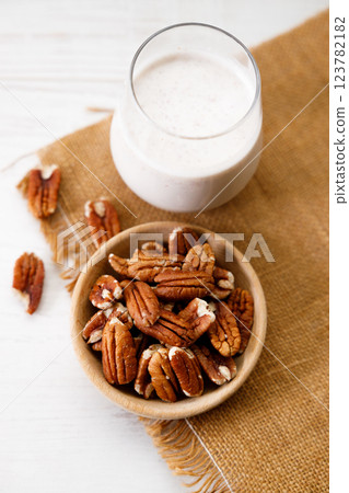 Pecan milk in a glass with raw pecan nuts on wooden table. Pecan milk in a glass with raw pecan nuts on wooden table. 123782182