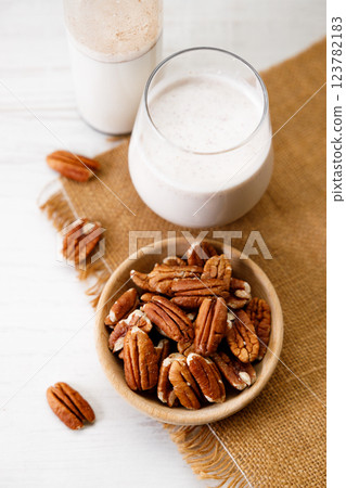 Pecan milk in a glass with raw pecan nuts on wooden table. 123782183