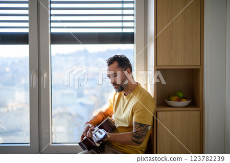 Diabetic man with CGM sensor on arm playing on guitar. 123782239