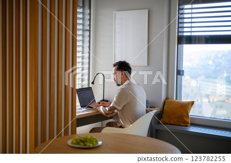 Man with CGM sensor on arm sitting at table and working on laptop. 123782255