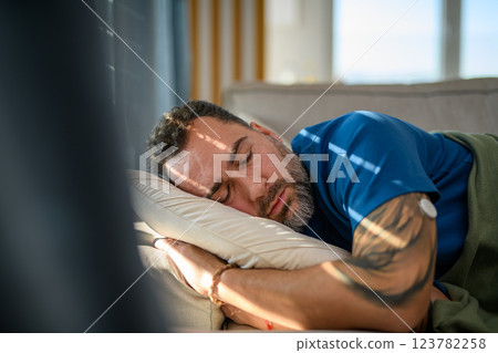 Diabetic man with CGM sensor on arm sleeping on sofa. 123782258
