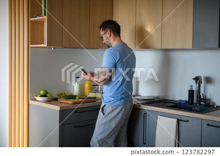Diabetic man with CGM sensor checking his blood sugar level while making healthy breakfast. 123782297