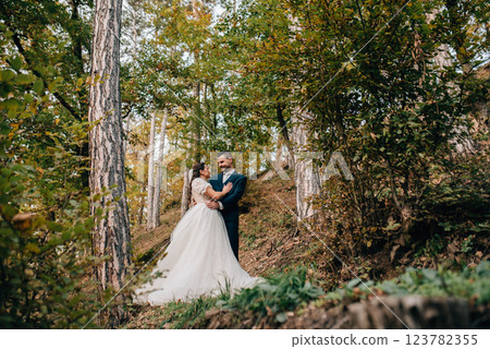 Portrait of beautiful bride and an elegant groom in nature, surrounded by a forest. 123782355