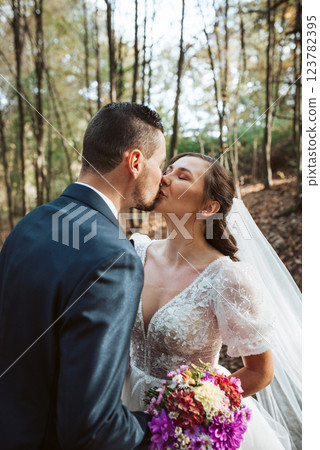 Portrait of bride and an elegant groom kissing in nature, surrounded by a forest. 123782395