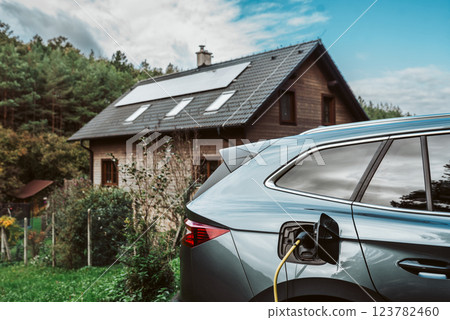 Electric car charging in front of house with solar panels on roof. Electric car charging in front of house with solar panels on roof. 123782460
