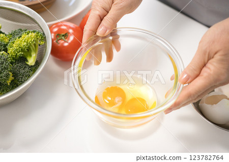 Middle-aged woman's hand holding freshly cracked eggs in a bowl Middle-aged woman's hand holding freshly cracked eggs in a bowl 123782764